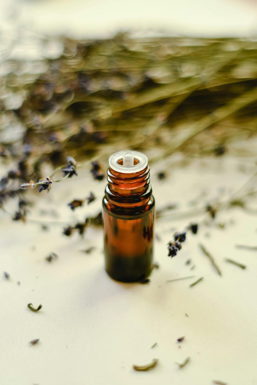Still life of a brown glass bottle among dried lavender flowers on a white surface.