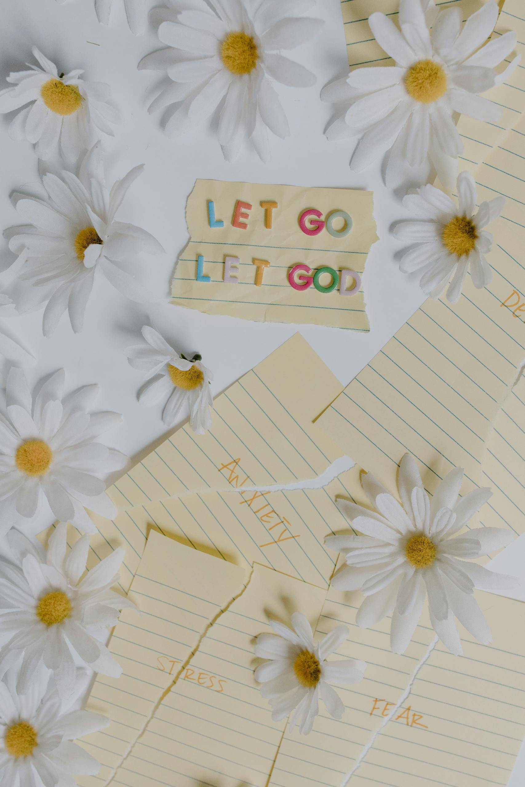Inspirational quote 'Let Go Let God' amid daisies and paper notes on stress and fear.